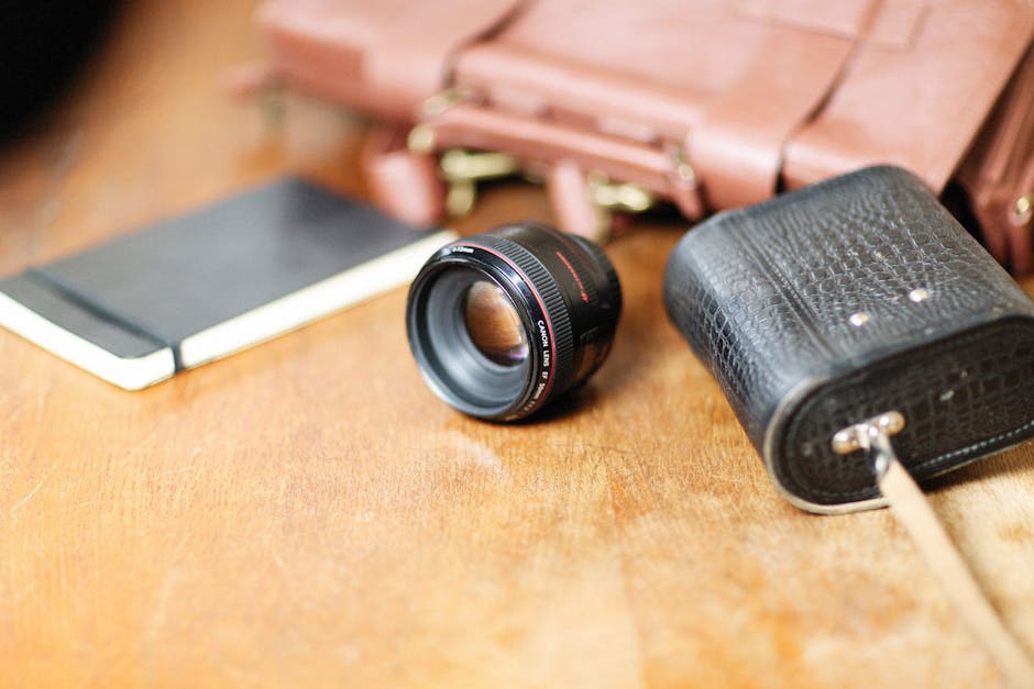 Camera lens, pouch, and leather bag on wooden surface.
