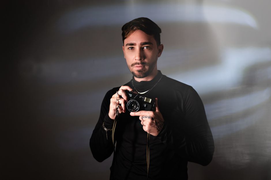 Portrait of a stylish male photographer holding a vintage camera in a studio setting.
